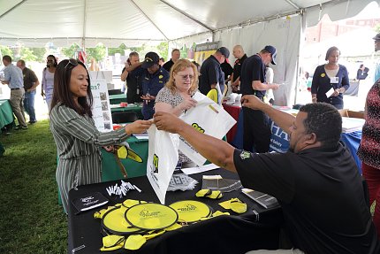 A couple of people accept totebags from person behind Miss Utility display table.