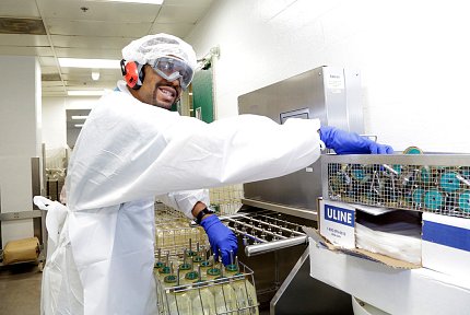 Man in labcoat, cap and gloves handles research materials and equipment.