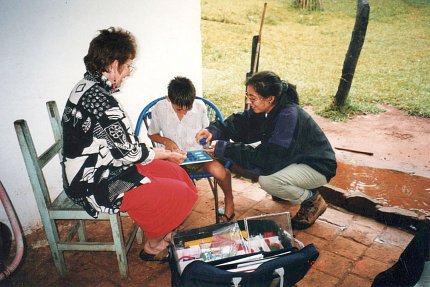 Schuster and Austin seated outside gather with a child over a short table