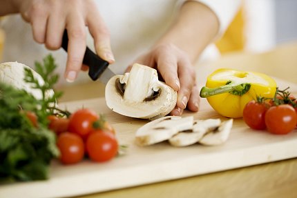 close-up view of hands holding large mushroom being sliced with cherry tomatoes in foreground and half yellow bell pepper alongside