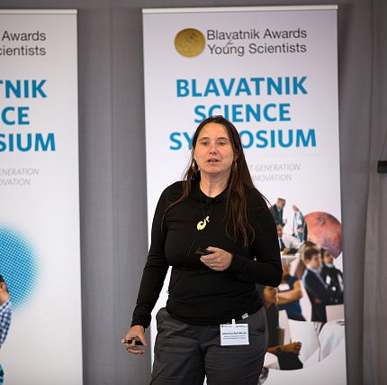 Roll-Mecak stands in front of Blavatnik Science Symposium banner