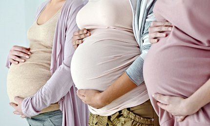 Three women place hands on their pregnant bellies.