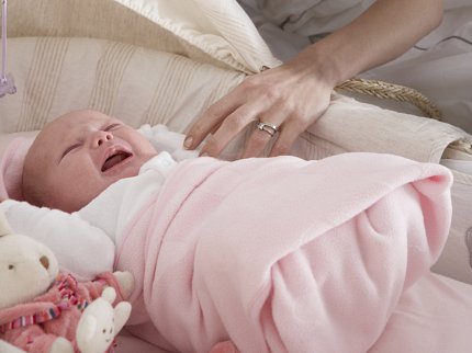 A mom's arm reaches toward a crying baby in a bassinet. 