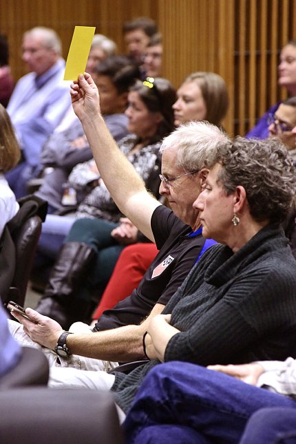 Seated in audience, man holds up yellow card.