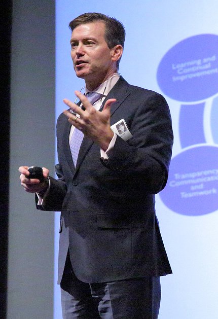 Pronovost speaks from stage with slide projected behind him.