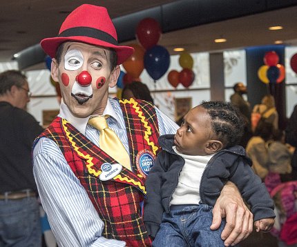 Circus clown cradles astonished young child.