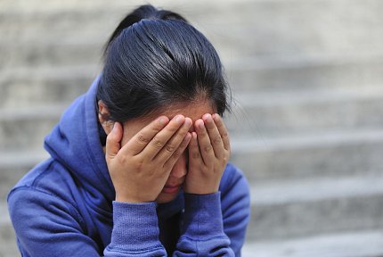 Young girl seated on outdoor stairs covers her face with both hands