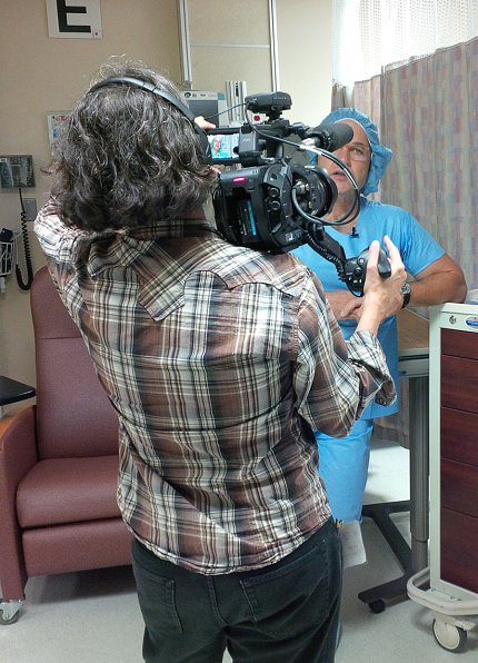 In blue scrubs, NHLBI's Dr. Tisdale talks on camera outside operating room in Clinical Center