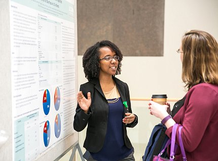 Diallo gestures toward poster as a visitor listens.