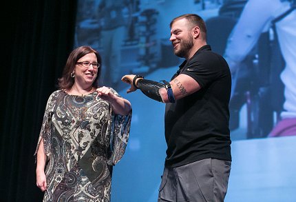 An audience volunteer helps Mills demonstrate features of his prosthetic arm.