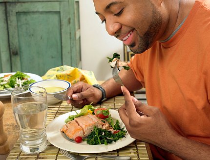 A man sits at a table at home eating a salmon salad.