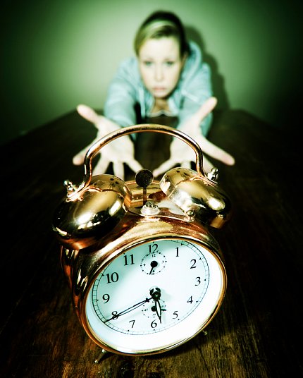 Young woman reaching out with both hands for alarm clock.