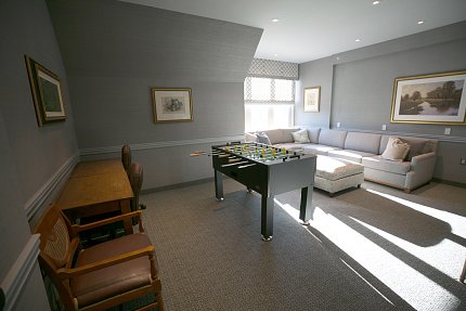 View of room with lounge chairs, sofa and Foosball table with sunlight coming through a corner window
