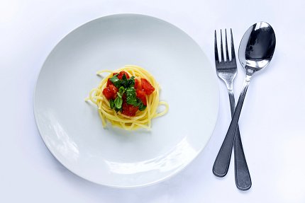 Spaghetti and red sauce on a white plate next to silverware