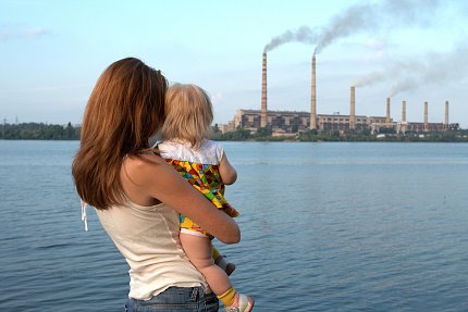 A mother and child look across a river towards a polluting power plant