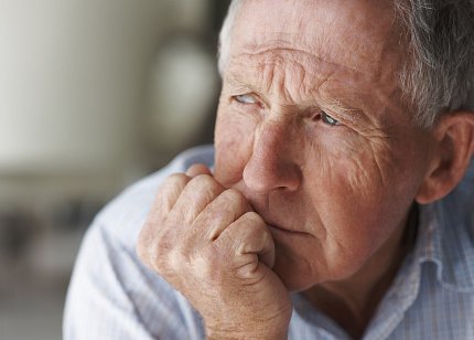 A grey-haired man looks thoughtfully into the distance 