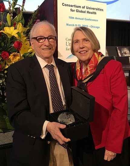 A smiling Dr. Bridbord and his wife stand in front of global health consortium poster.