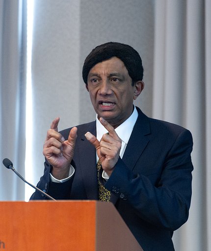 Dr. Manji is gesturing at the podium.