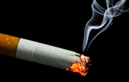 A lit cigarette burning on a black background.