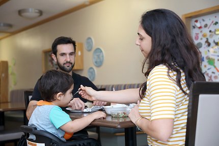 Inn mom feeds youngster as dad watches.