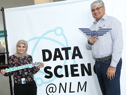 Two attendees stand in front of a sign that reads "Data Science @ NLM"