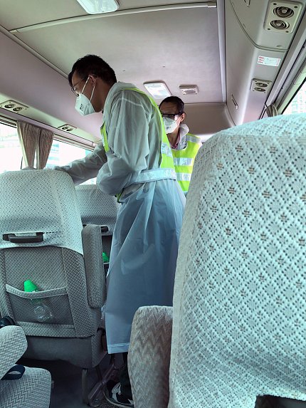 View of masked, gowned man checking the temperature of a bus rider