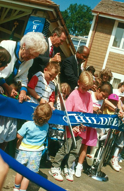 President Bush cuts a blue ribbon with giant scissors, while children look on