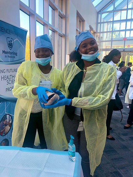 Two young women in surgical gowns hold a model of human brain.