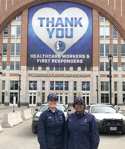 Two female Commissioned Corps members in uniform stand side by side in front of thank you banner.