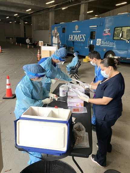 Workers in protective masks and gear assemble testing supplies around a table.