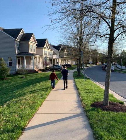 Seen from behind, 2 foster children walk together along the sidewalk.