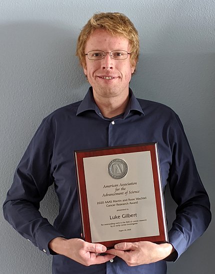 A smiling Gilbert stands holding his plaque.
