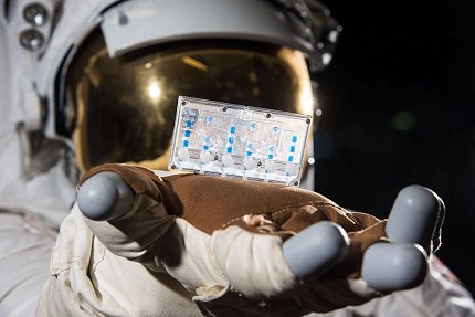 A person in an astronaut suit holds up a tissue chip