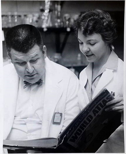 Black &amp; white image of Stohlman and Judith McKay Sides looking at book