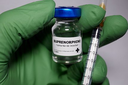 A green-gloved hand holds a needle and a bottle labeled Buprenorphine