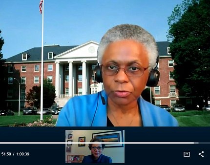 Dr. Marie Bernard speaks virtually in front of image of Bldg. 1 on NIH's campus.