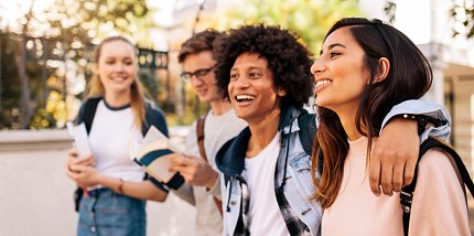 Four smiling teenagers walk arm in arm.