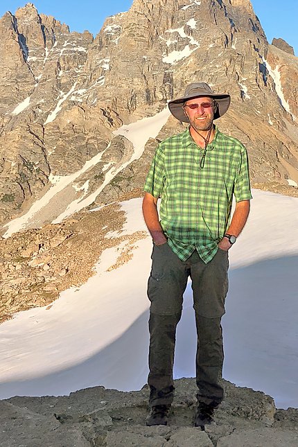 Kercher in sunshades and sunhat with wide brim, with mountains behind him