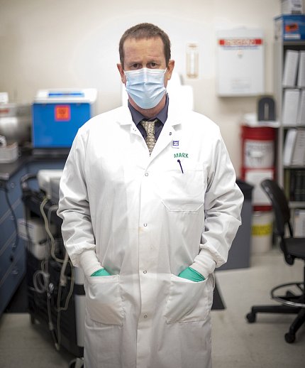 Pandori stands in long white lab coat and mask in the lab.