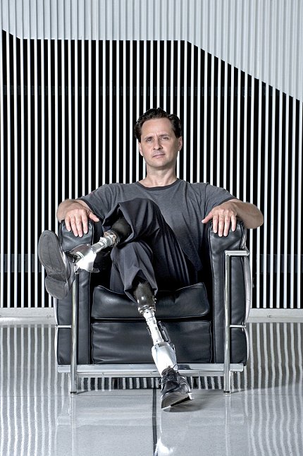 Herr sits facing forward with his legs crossed.