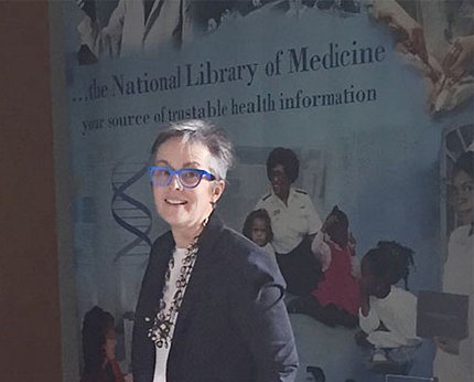 Adams stands in front of NLM sign in Natcher that reads: "your source of trustable health information."