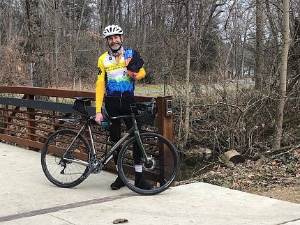 Bicycle, with male rider standing beside, at one side of a bridge