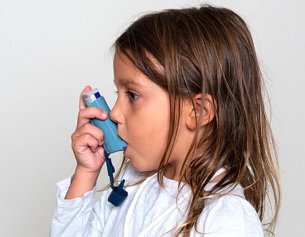 A young girl holds a blue inhaler to her mouth.
