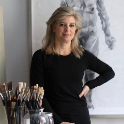 Hill-Edgar stands in front of artwork mounted on wall and behind a table with paintbrushes in foreground