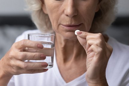 An older woman holds a pill in one hand a glass of water in the other.