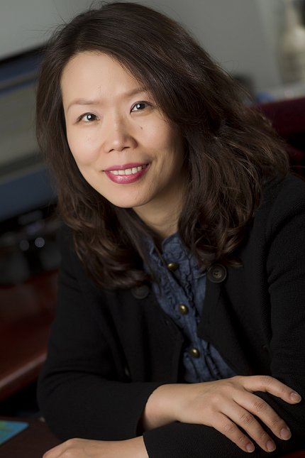 A smiling Mi-Kyung Song sits with arms resting on table