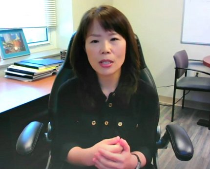 Song sitting, hands folded, in front of her office desk.