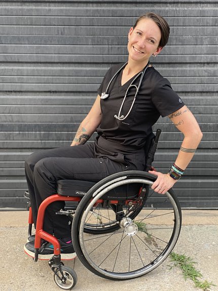 Mason sits in her red wheelchair wearing black scrubs