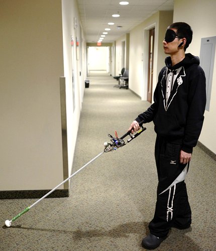 Man in blindfold with cane device in hand stretched out in front of him