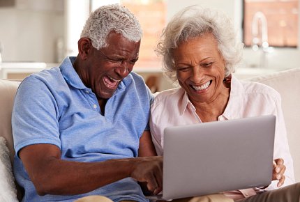 Gray-haired Black couple smiling behind a laptop